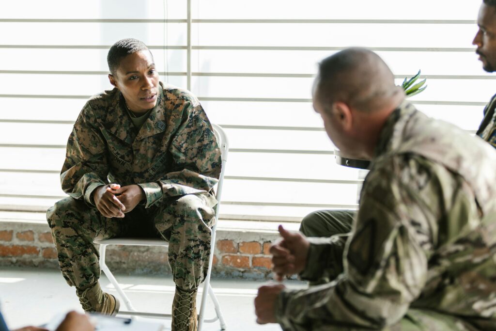 Veterans in uniform seated in a discussion circle, listening attentively during a support or intake session